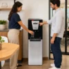 Dispensador Royal Aqua Freeze en cocina de oficina mexicana, persona presionando botón de agua caliente y otra llenando vaso